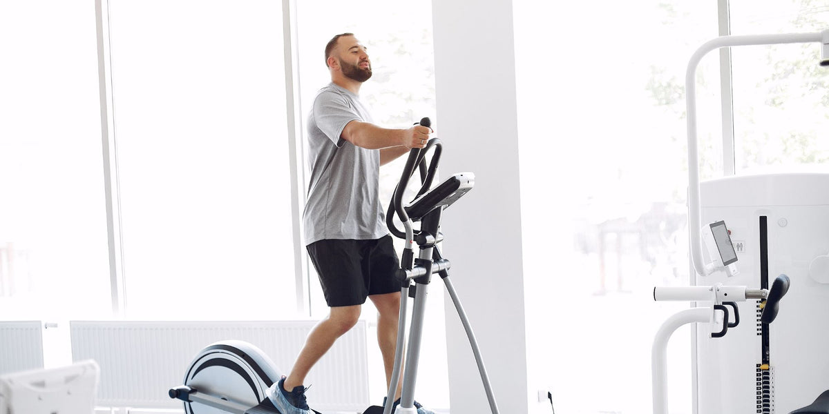 Bearded man exercising on elliptical machine in bright gym